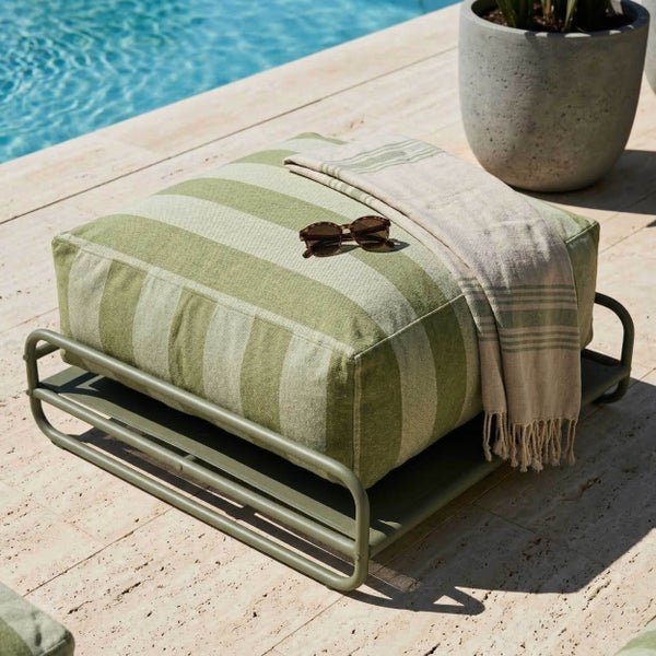 Gestreiftes Bodenkissen auf einem grünen Metallgestell im Außenbereich am Pool mit Sonnenbrille und Handtuch.
