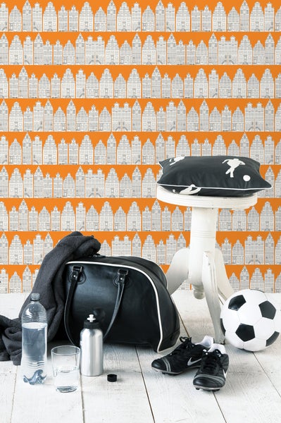 Szene mit Sporttasche, Fußball und Fußballschuhen vor einer Wand mit Hausmuster-Tapete