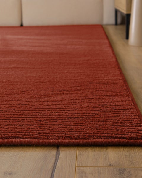 Strukturierter Teppich mit kurzem Flor und gerippter Oberfläche in Rot auf Holzfußboden.