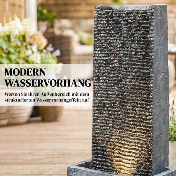 Moderner Gartenbrunnen als Säule mit strukturierter Oberfläche und Wasservorhang-Effekt in einem hellen Außenbereich.