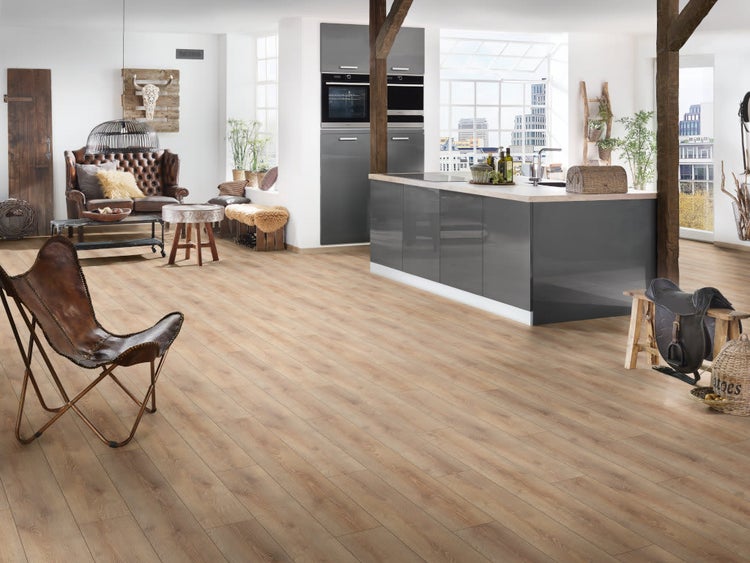 Offener Wohnbereich mit modernem Laminatboden in Holzoptik, kombiniert mit einer Kücheninsel und einem Sofa im Loft Stil.