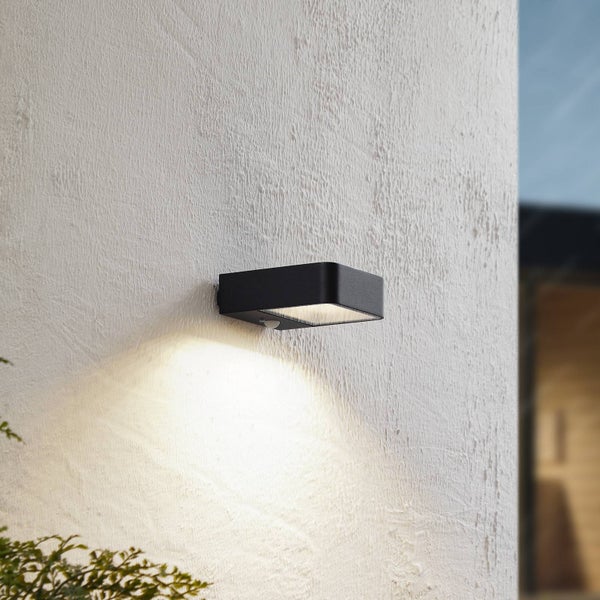 Moderne rechteckige LED-Außenwandleuchte in Schwarz mit Bewegungssensor, montiert an einer weißen strukturierten Wand.
