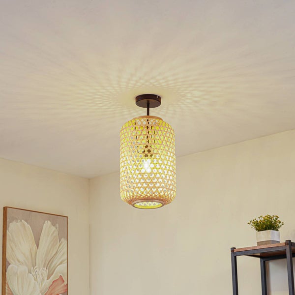 Heller Raum mit moderner Bambus-Deckenleuchte, gelber geflochtener Schirm wirft Lichtmuster an die Decke, inklusive Wandbild und Pflanze.