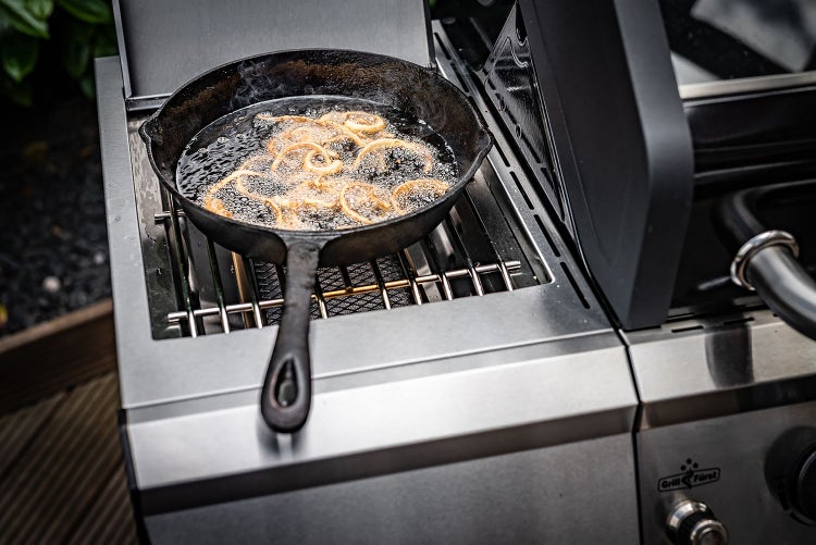Gusseisenpfanne mit frittierten Zwiebelringen auf einem Grill