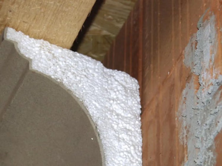 Nahaufnahme von weißer Styropordämmung zwischen einem Holzbalken, einem gewölbten Bauelement und einer Ziegelwand.