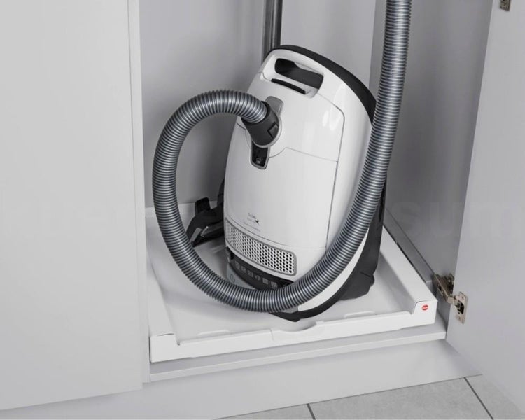Staubsauger auf einem weißen ausziehbaren Tablar in einem Schrank verstaut.