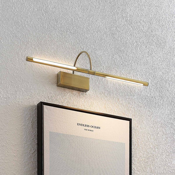 Moderne LED-Bilderleuchte aus Messing an einer strukturierten Wand über einem gerahmten Bild.