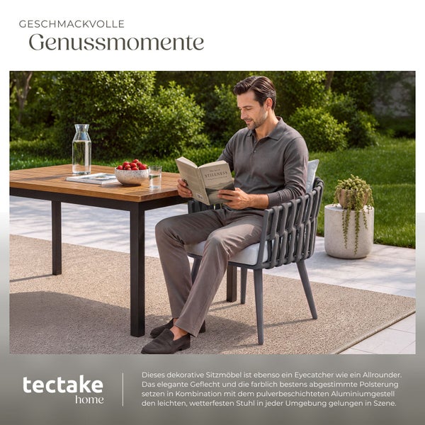 Ein Mann liest ein Buch auf einem modernen Gartenstuhl mit Geflecht aus Aluminiumgestell an einem Gartentisch auf einer Terrasse.