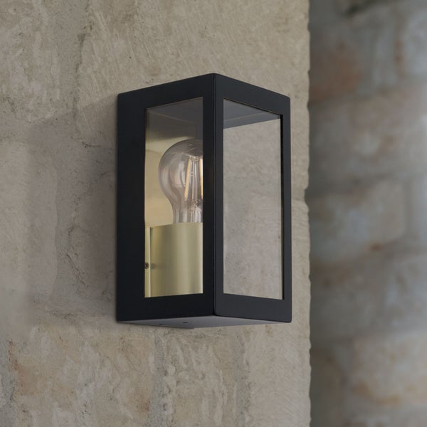 Rechteckige Außenwandleuchte aus schwarzem Metall und Glas mit sichtbarem Leuchtmittel montiert an einer Steinwand.