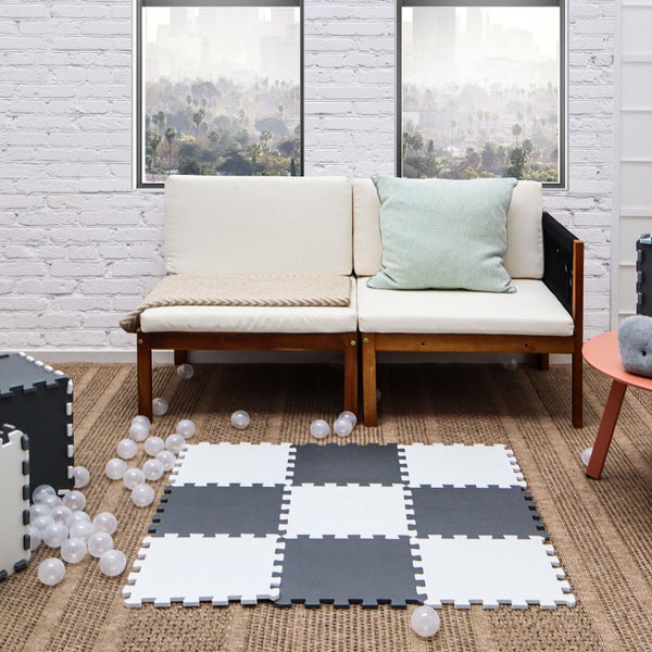 Wohnzimmer mit Sofa, Kissen und Spielteppich aus zusammensteckbaren Schaumstoffmatten im Schachbrettmuster auf dem Boden.