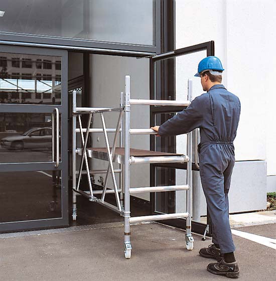 Ein Arbeiter schiebt ein Aluminiumfahrgerüst durch eine Glastür.
