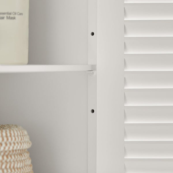 Detailansicht eines weißen Badschranks mit Regalböden und Lamellentür