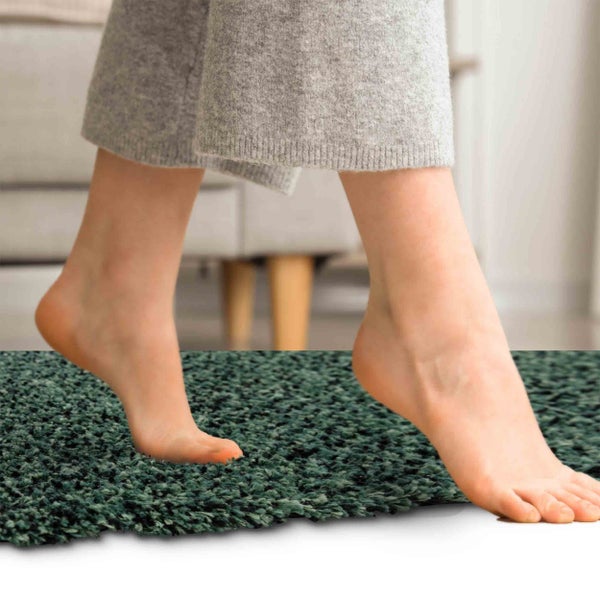 Barfuß auf einem weichen, dunkelgrünen Hochflor-Teppich oder Badeläufer im Innenbereich.