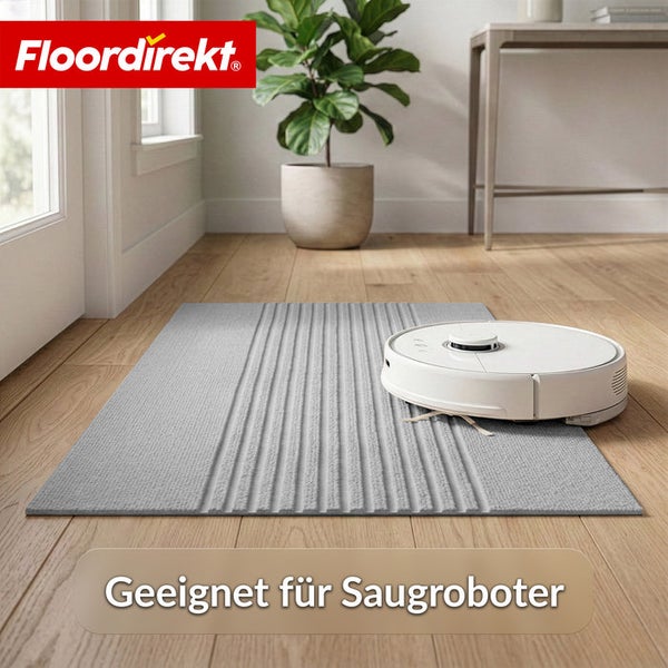 Grauer Teppich mit Rippenstruktur auf hellem Holzboden, befahren von einem weißen Saugroboter in einem hellen Wohnzimmer. Floordirekt Logo.