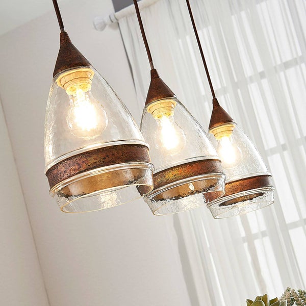 Dreiflammige Pendelleuchte mit gläsernen Lampenschirmen und rustikalen Metallelementen vor einem hellen Vorhang.
