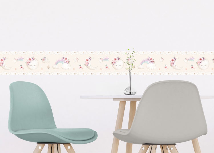 Selbstklebende Tapetenbordüre mit Monden, Regenbogen, Sternen und Blumen in einem hellen Kinderzimmer über einem Tisch mit Stühlen.