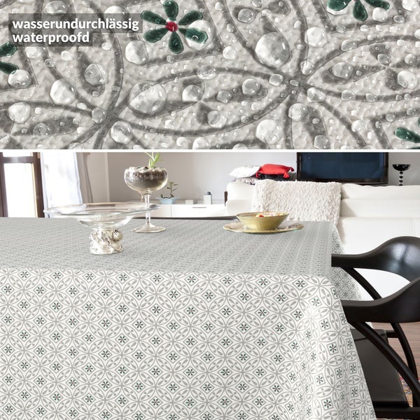 Wasserundurchlässige Tischdecke mit geometrischem Blumenmuster auf einem Esstisch in einem hellen Zimmer. Nahaufnahme zeigt Wassertropfen.