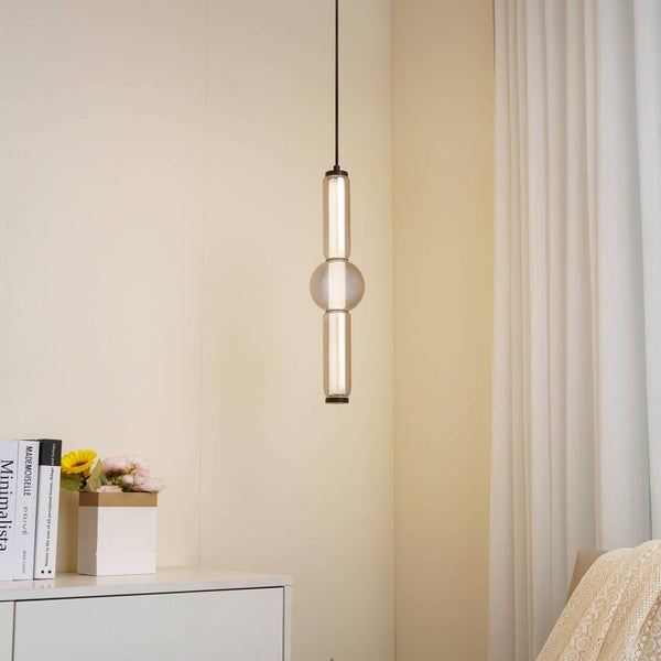 Moderne Pendelleuchte mit röhrenförmigem Design und zentraler Glaskugel an einem schwarzen Kabel in einem hellen, minimalistischen Zimmer.