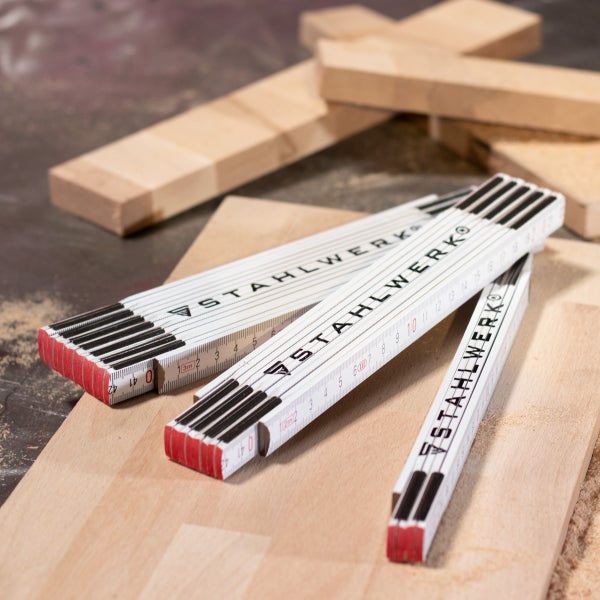 Drei zusammengeklappte Stahlwerk Gliedermaßstäbe aus Holz auf Holzbrettern in einer Werkstatt.