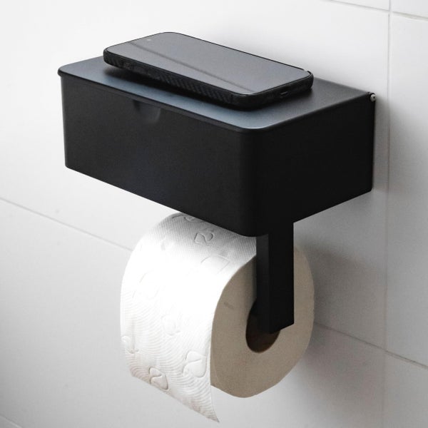 Toilettenpapierhalter mit Ablage aus Metall, montiert an einer gefliesten Wand mit Toilettenpapierrolle und Smartphone als Ablage