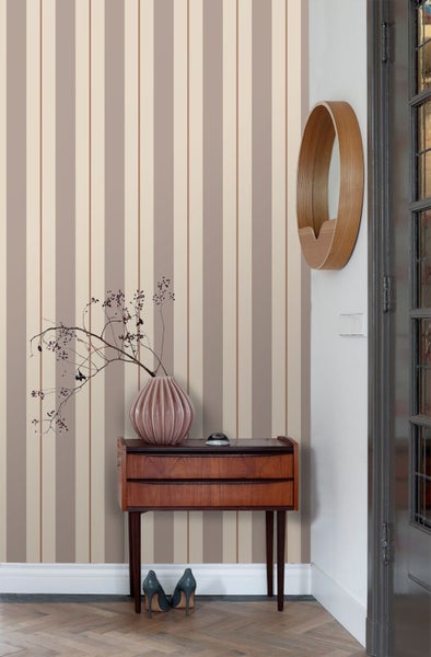 Gestreifte Vliestapete in einem Raum mit Holzkommode, Keramikvase und rundem Wandspiegel.