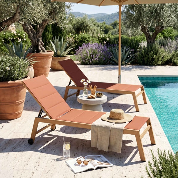 Zwei Gartenliegen aus Holz mit terracottafarbenem Bezug an einem Pool, umgeben von Olivenbäumen und Lavendel auf einer hellen Steinterrasse.