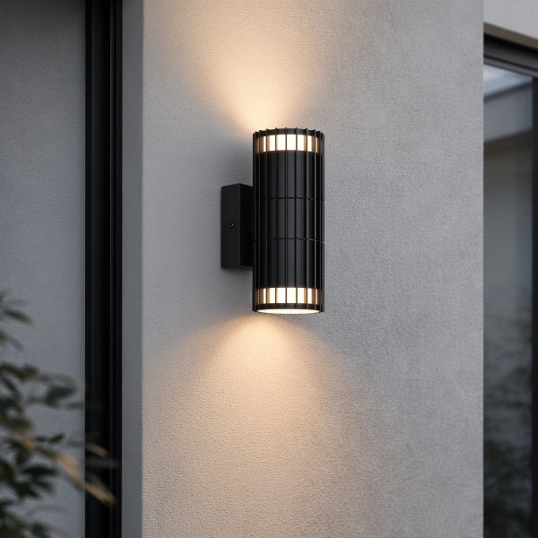Schwarze zylindrische Außenwandleuchte mit Licht nach oben und unten, geripptes Metalldesign an einer Fassade.