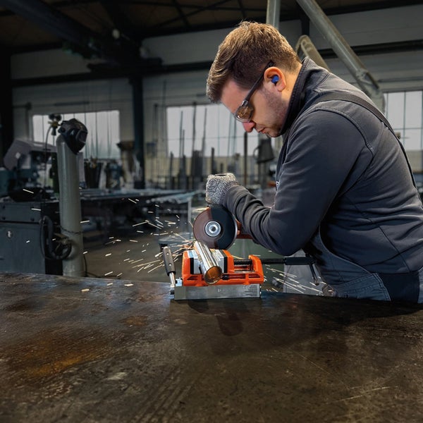 Handwerker verwendet einen Winkelschleifer-Ständer zum Trennen eines Metallrohres in einer Werkstatt mit sichtbarem Funkenflug.