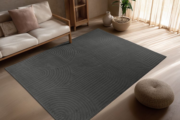 Ein moderner rechteckiger Teppich mit geometrischem Linienmuster in einem Wohnzimmer mit Holzmöbeln und hellem Holzboden.