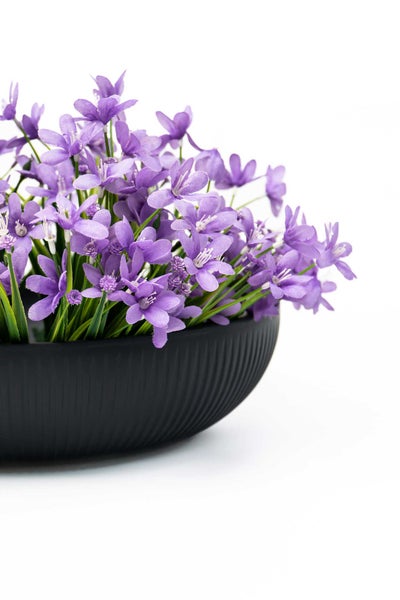 Künstliche lilafarbene Blumen in einer schwarzen geriffelten Schale