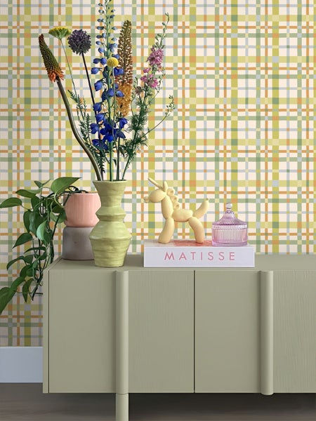 Moderne Inneneinrichtung mit einer karierten Tapete in verschiedenen Farben hinter einem hellgrünen Sideboard mit Dekorationsartikeln und bunten Blumen.
