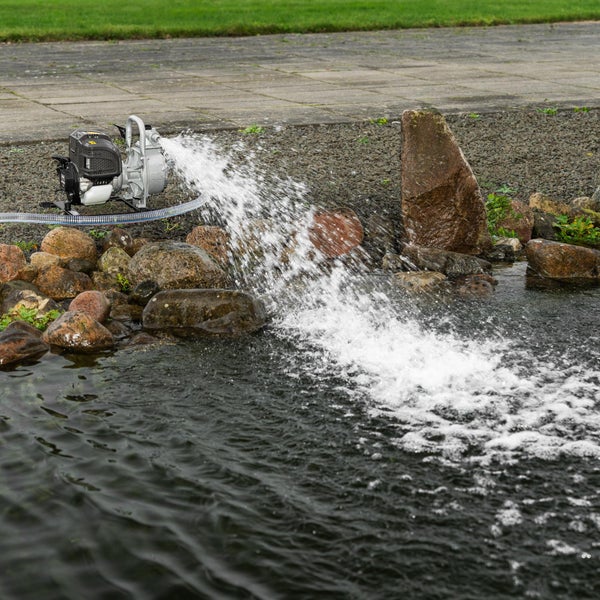 Benzin Wasserpumpe fördert Wasser in einen Gartenteich mit Steinen am Ufer