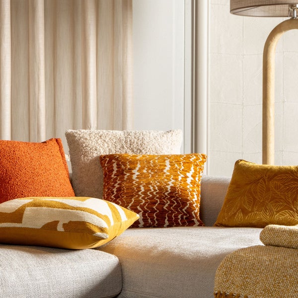 Dekorative Kissen auf einer Couch mit verschiedenen Mustern und Texturen in einem hellen, modernen Wohnraum.