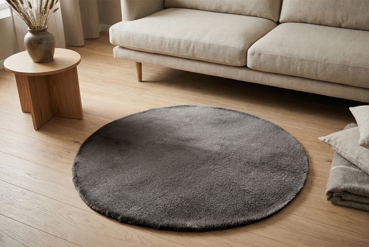 Runder Teppich in einem modern eingerichteten Wohnzimmer mit Sofa und Holztisch auf einem Holzboden.