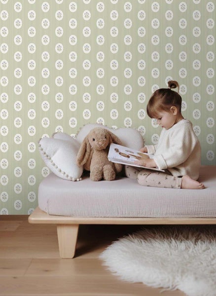 Vliestapete mit Blumen- und Streifenmuster in einem hellen Kinderzimmer mit einem Kind auf einem Bett und einem Stoffhasen.