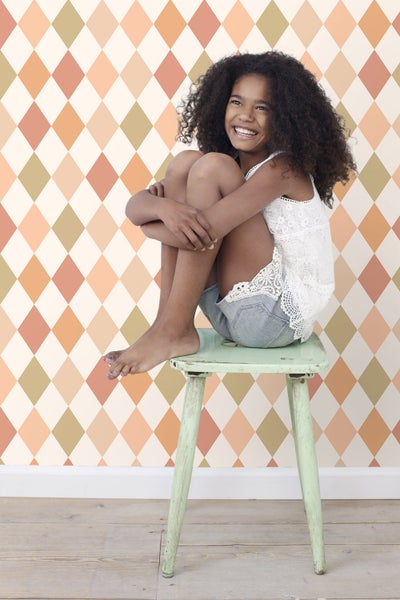 Mädchen sitzt auf einem Hocker vor einer Wand mit Rautenmuster.