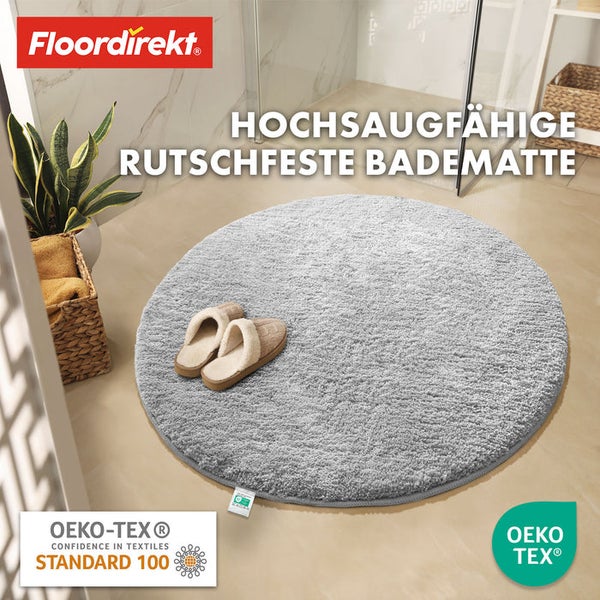 Runde, graue Badematte mit Hausschuhen im Badezimmer und Floor direkt Logo