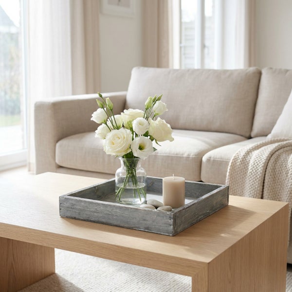 Dekoratives Holztablett mit Glasvase, Blumen und Kerze auf einem Holztisch in einem hellen Wohnzimmer mit Sofa.