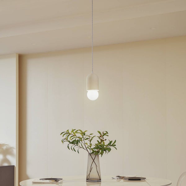 Minimalistische Pendelleuchte in Weiß mit runder Glühbirne, hängend über einem Tisch mit Glasvase und grünen Zweigen in einem hellen Raum.