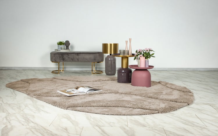 Wohnzimmer Interieur mit einer gepolsterten Sitzbank, Beistelltischen, Tischleuchte, Dekoration und einem runden Teppich auf einem Fliesenboden.