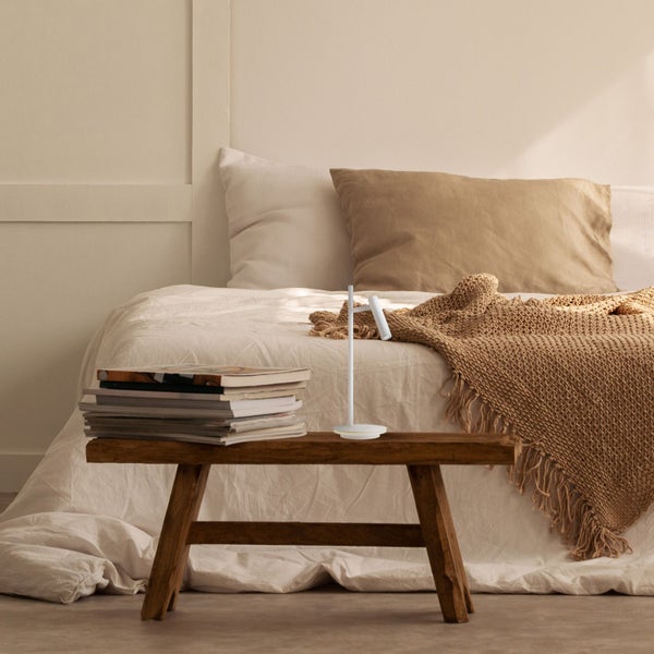 Schlafzimmerszene mit Bett, Holzhocker, Lampe und Büchern für eine gemütliche Atmosphäre.