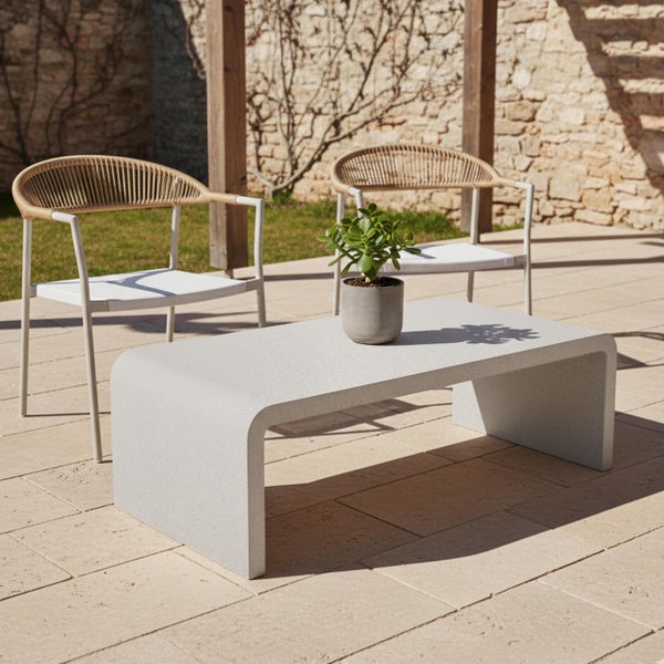 Modernes Gartenmöbel-Set auf Steinterrasse mit Betoncouchtisch und zwei Stühlen mit Seilbespannung vor einer Natursteinmauer.