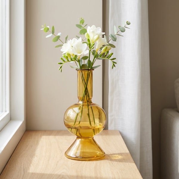 Dekorative Glasvase in Flaschenform mit Blumenstrauß auf einem Holztisch vor einem Fenster