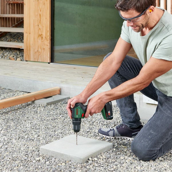 Mann bohrt mit Akku-Bohrschrauber ein Loch in eine Steinplatte im Außenbereich.