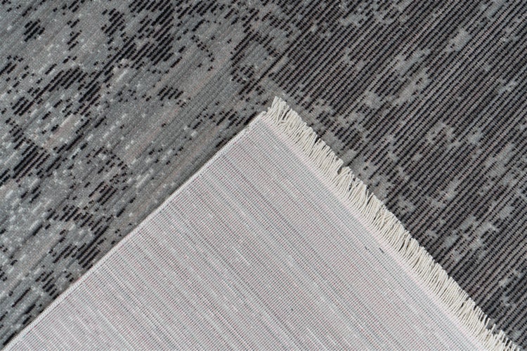 Teppich mit Vintage-Muster in Grau und Schwarz, Detailansicht der Unterseite und Fransen an einer umgeschlagenen Ecke.