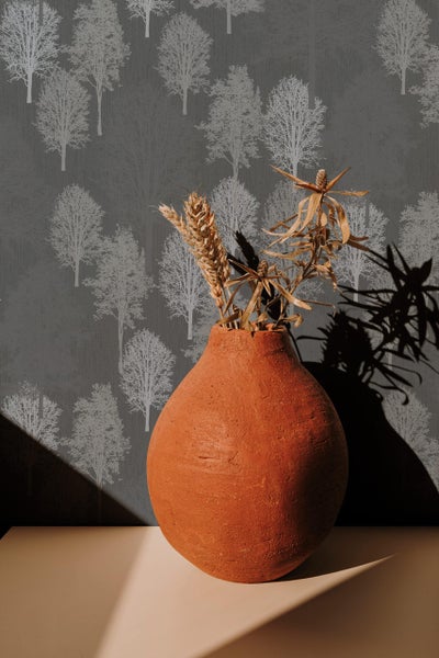 Strukturierte Tapete mit Waldmotiv im Hintergrund und eine Tonvase mit Trockenblumen im Vordergrund.