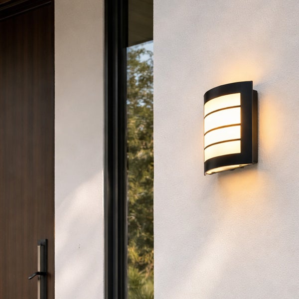 Moderne schwarze Außenwandleuchte mit warmweißem Licht, montiert an einer weißen Wand neben einer dunklen Holztür.