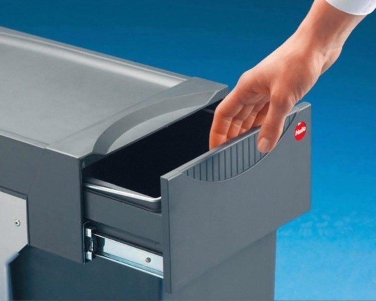 Hand öffnet einen grauen Abfallsammler-Auszug mit Hailo Logo und Teleskopschiene aus Metall.