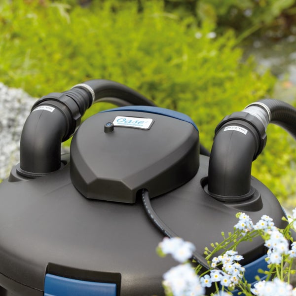Oase Teichdruckfilter mit zwei Schlauchanschlüssen und Oase Logo in einer Gartenumgebung.
