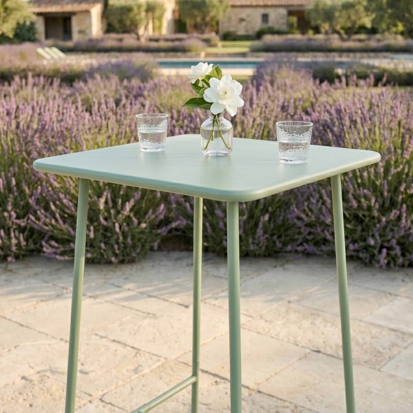 Quadratischer Gartentisch aus Metall auf einer Steinterrasse vor einem Lavendelfeld, dekoriert mit Gläsern und einer Vase mit weißen Blumen.